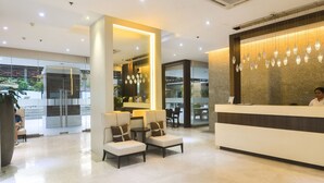 Un moderno vestíbulo de hotel con mostrador de recepción, zona de estar y puertas de cristal que dan a un comedor.