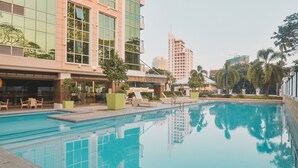 Una piscina con sillas de descanso y un edificio con ventanas amplias y balcones.