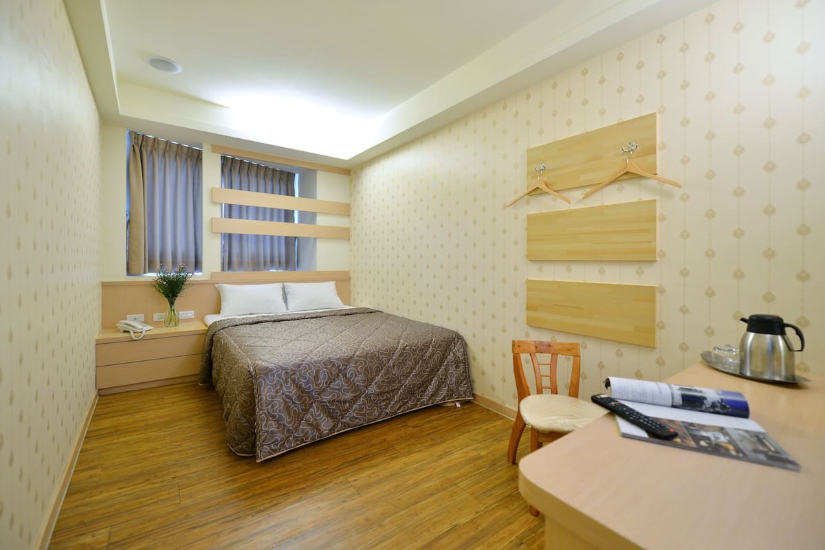 Quarto de hotel com cama, escrivaninha com cadeira, máquina de café e janela com cortinas.