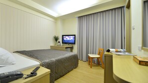 A hotel room with a bed, bedside table with a phone and remote, a desk with a chair, a television, and a window with curtains. - Ing Wang Hotel (Tainan)
