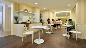 A modern dining area with round tables and white chairs, a kitchen counter with various items, and a large mirror on the wall. - Ing Wang Hotel (Tainan)