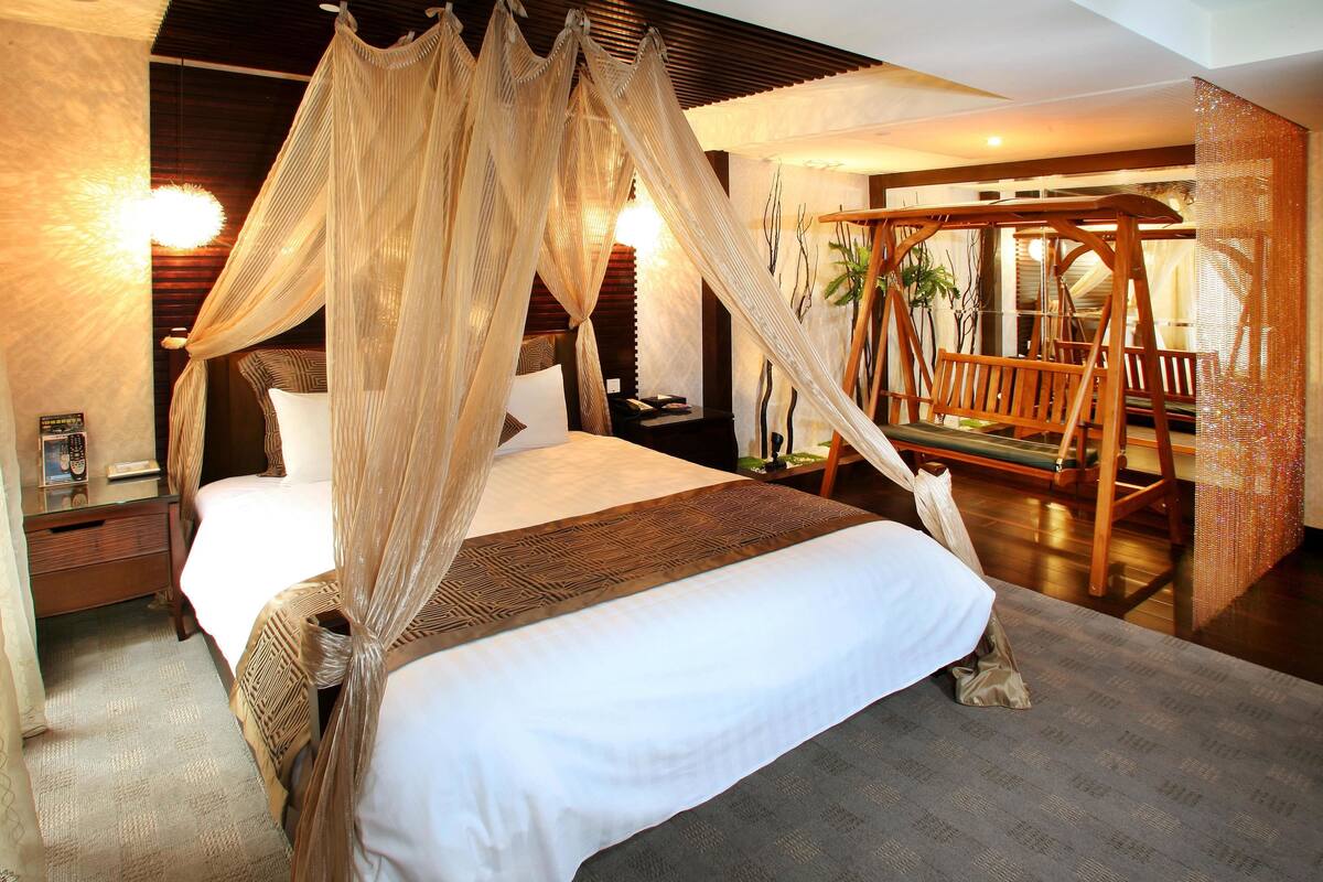 Quarto com cama de dossel, um balanço de madeira e mesa de cabeceira com abajur.