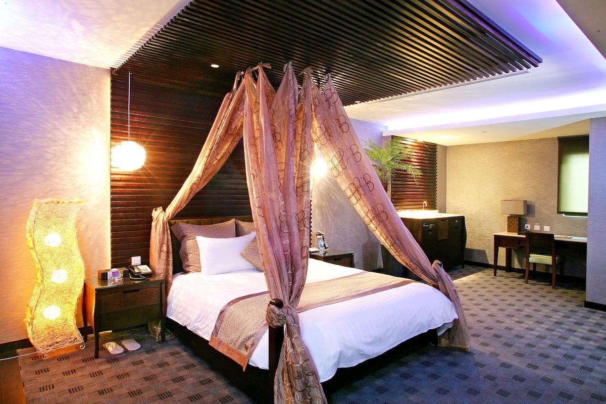 Quarto de hotel com cama de dossel, escrivaninha e uma cadeira.