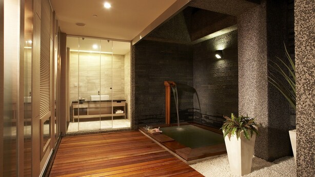 Un baño moderno con suelo de madera, cabina de ducha de vidrio, bañera independiente y una planta en maceta.