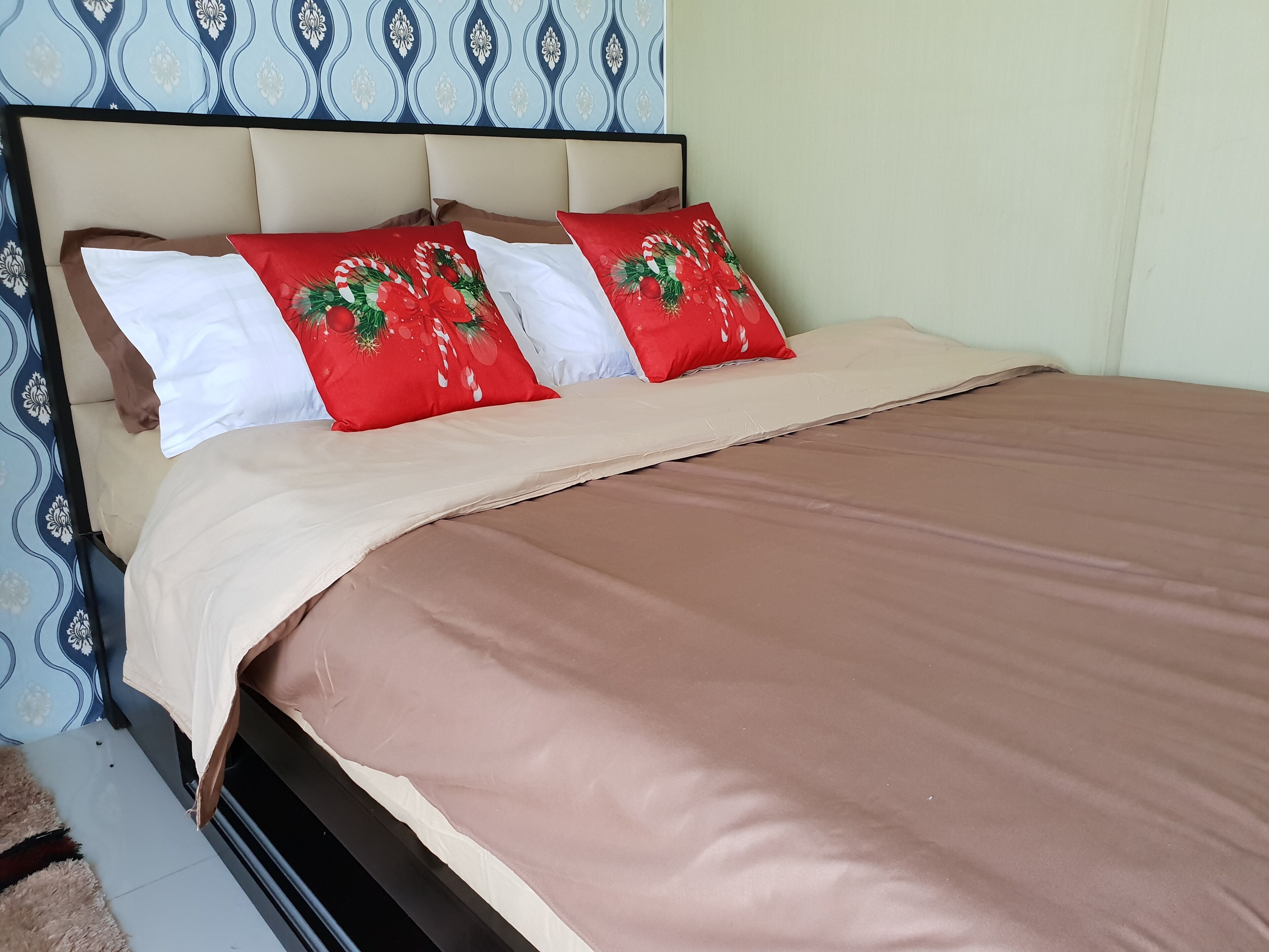 Ein Bett mit einem beige gefärbten Kopfteil, weißen und roten Kissen sowie einer braunen Bettdecke.