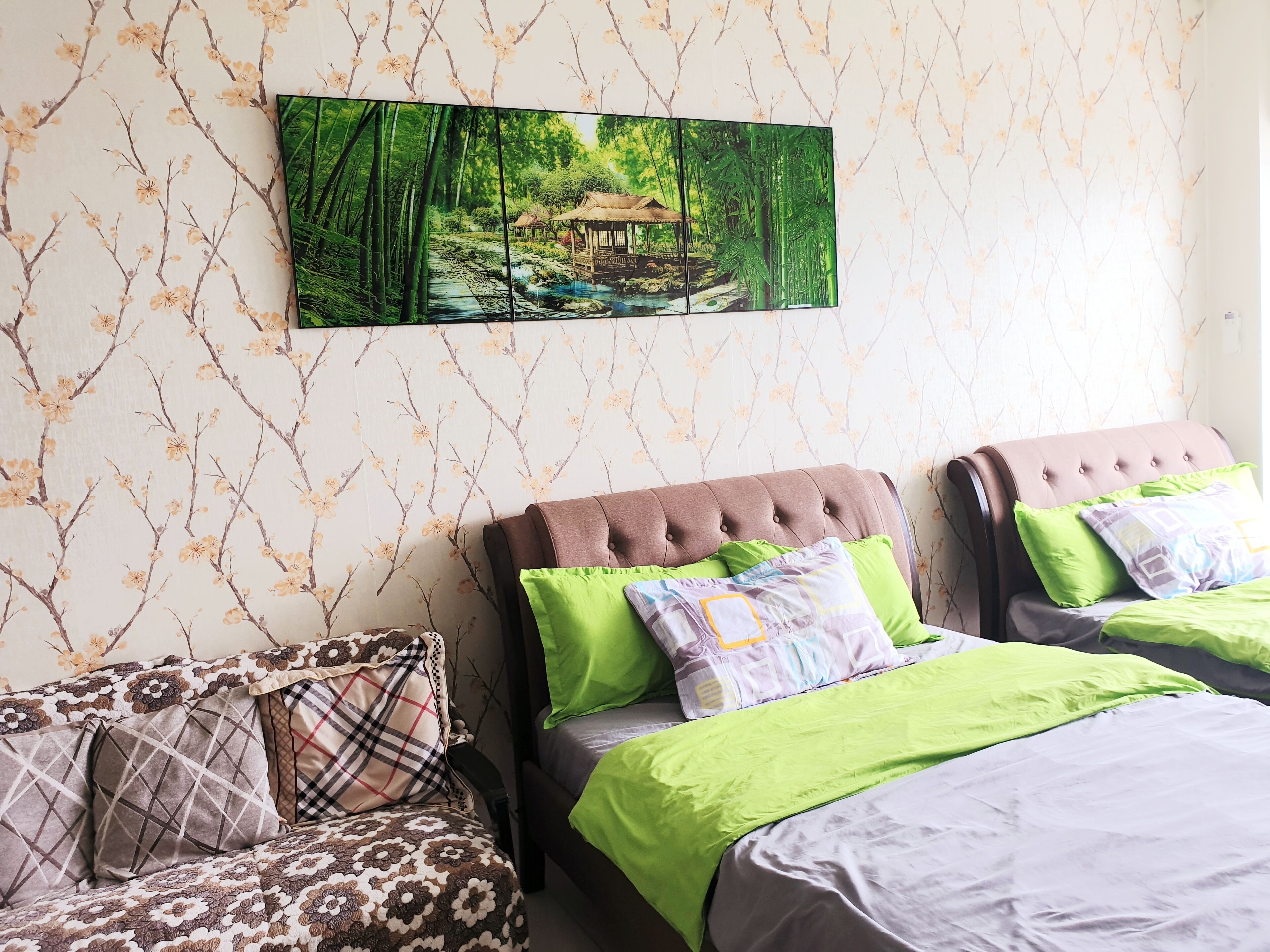 A bedroom with two beds, a sofa, and a wall-mounted painting of a bamboo forest.