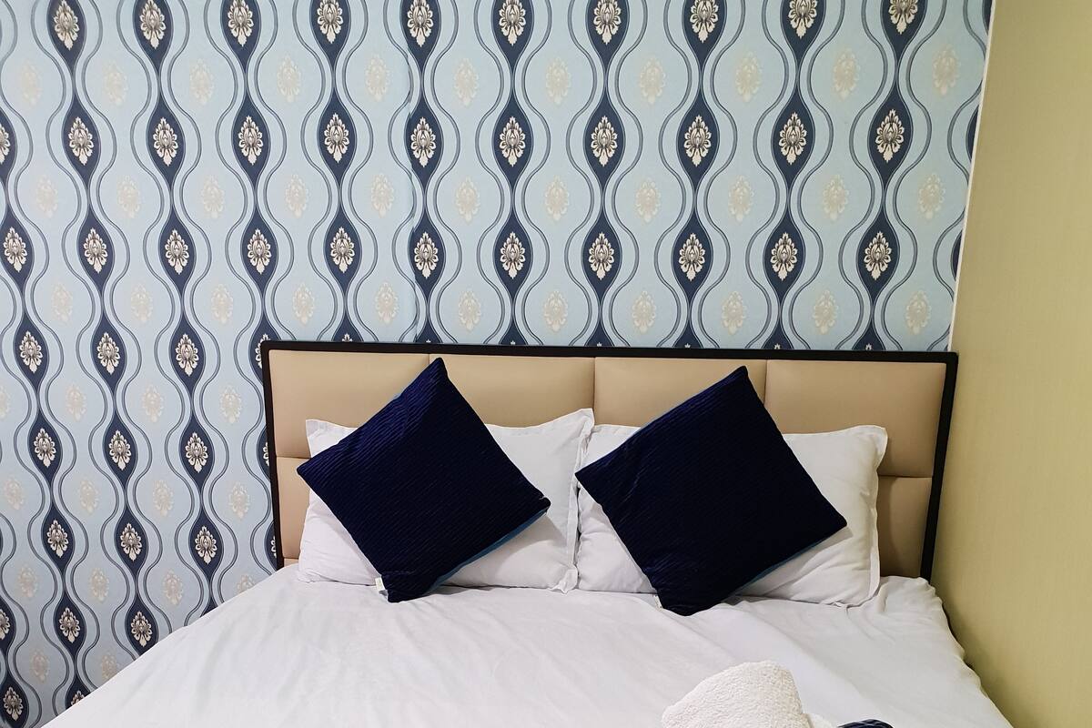 A neatly made bed with white linens, two dark blue pillows, and a folded white towel on the bed.