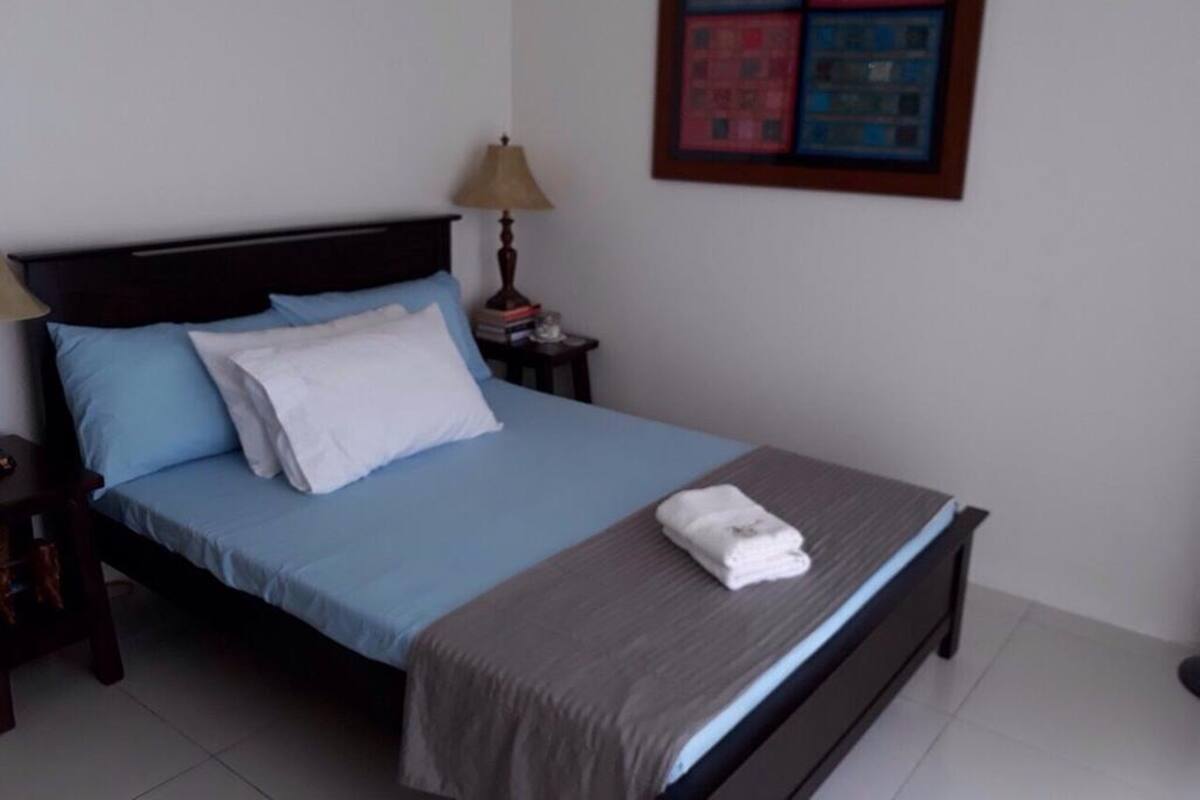 A neatly made bed with blue and white bedding, a bedside lamp, and a framed artwork on the wall.