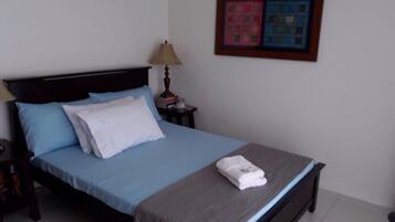 A neatly made bed with blue and white bedding, a bedside lamp, and a framed artwork on the wall.