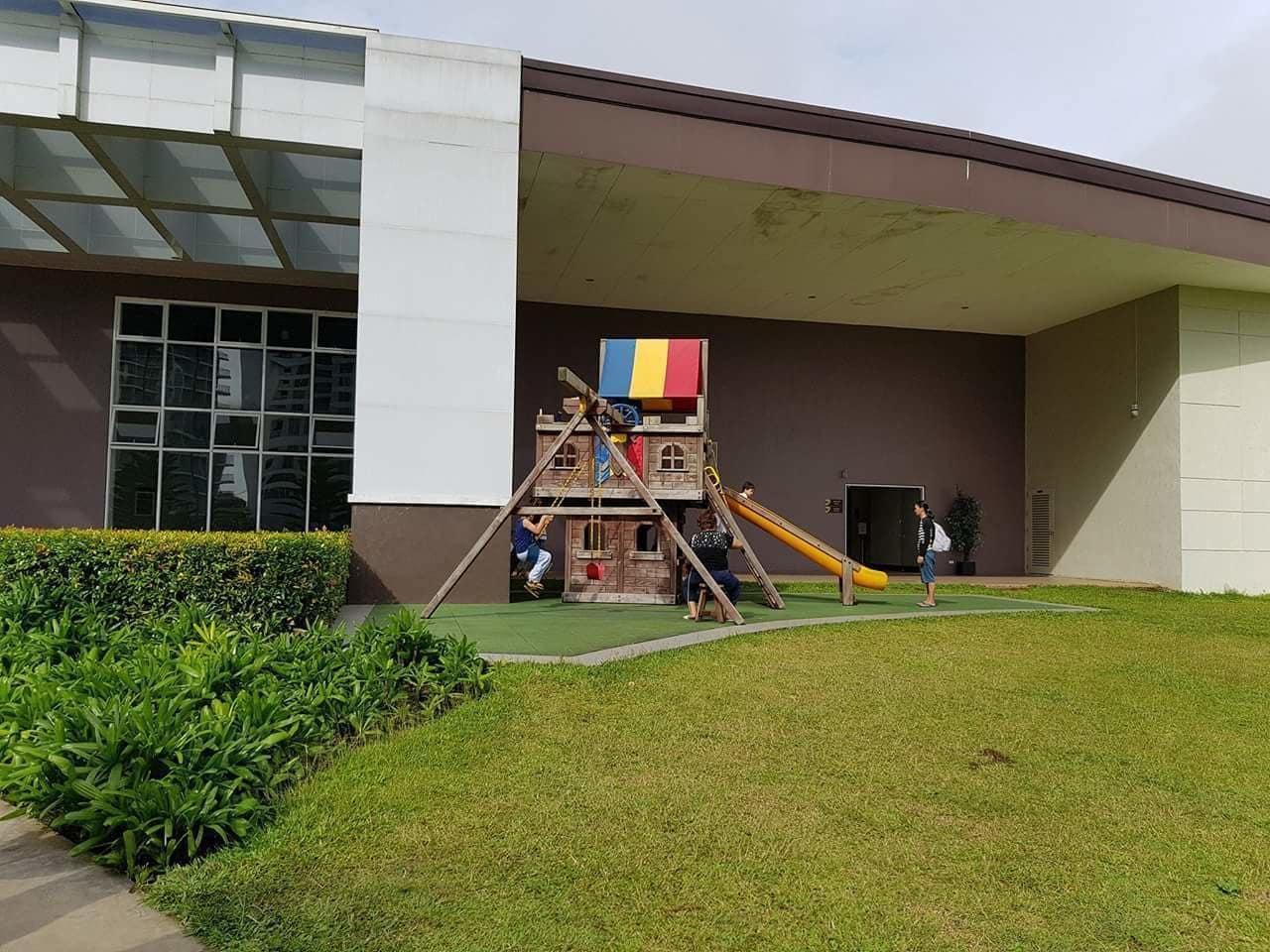 Un parque infantil con una estructura para escalar y un tobogán frente a un edificio.