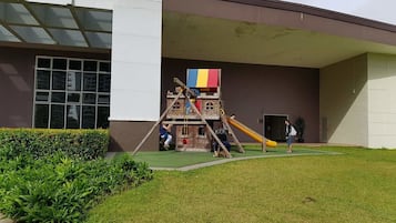 Un parque infantil con una estructura para escalar y un tobogán frente a un edificio.