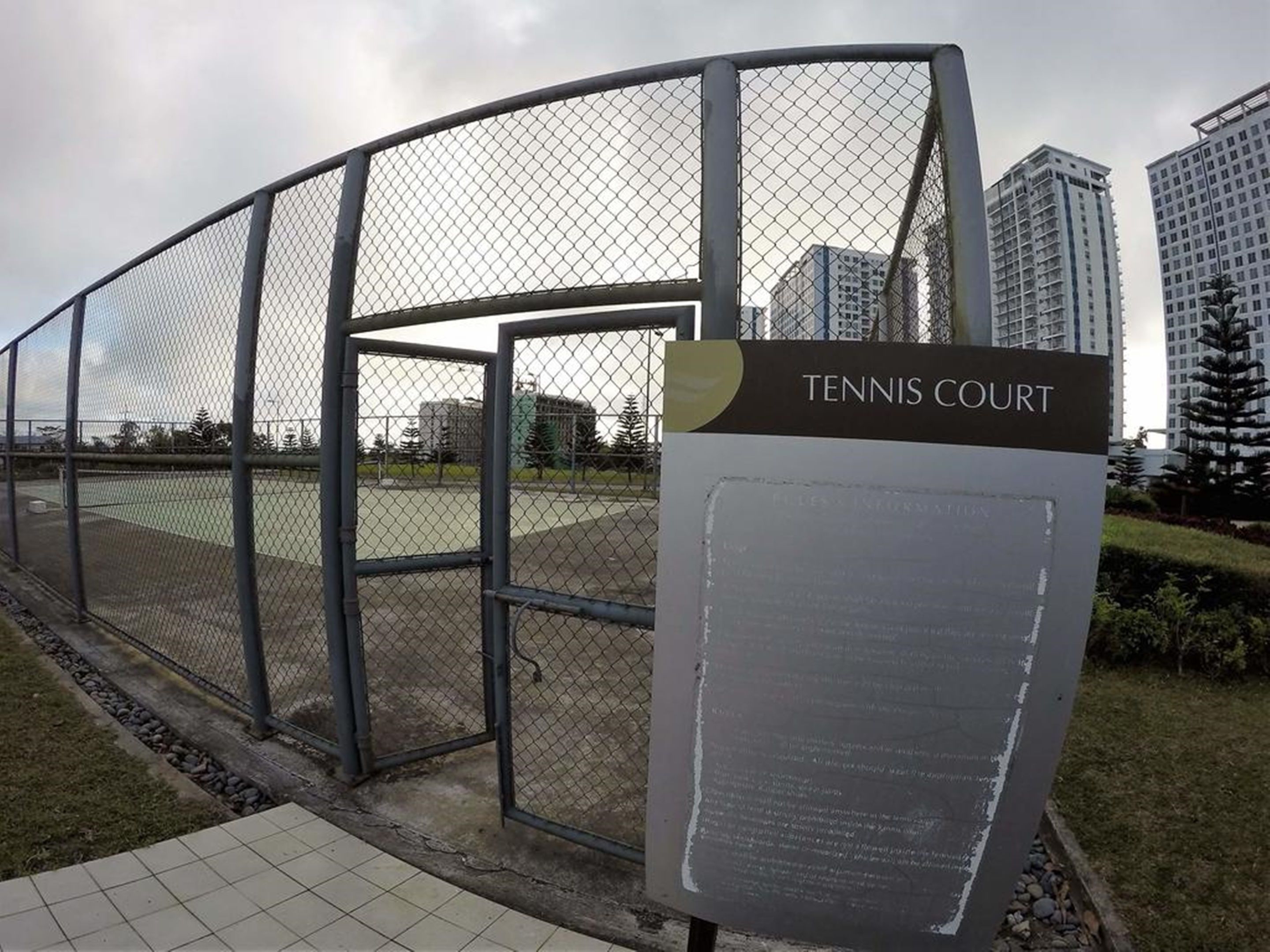 A tennis court with a metal fence and a sign indicating its name.