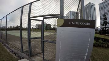 A tennis court with a metal fence and a sign indicating its name.