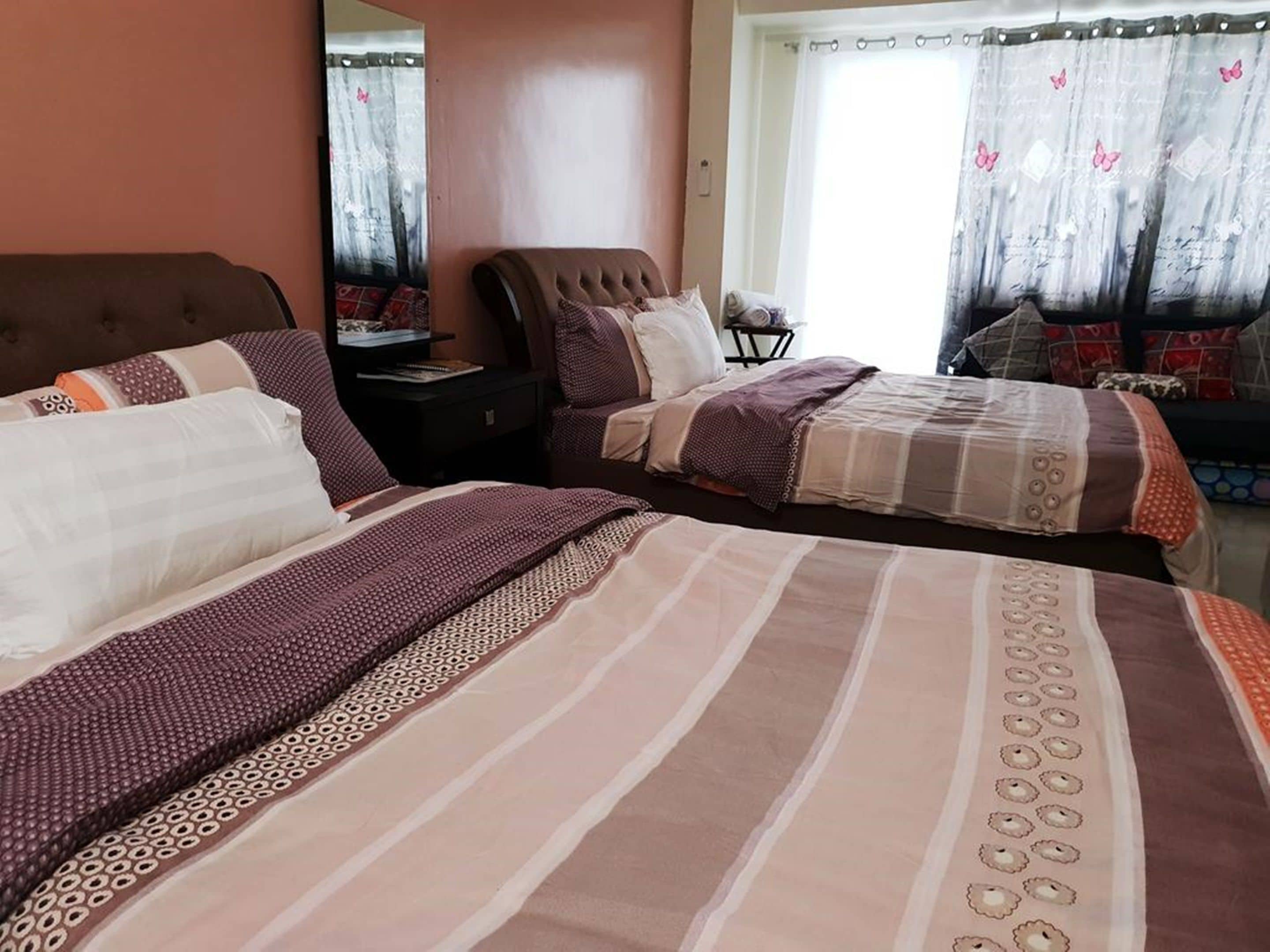 Quarto com duas camas, uma mesa de cabeceira, uma cadeira e janela com cortinas.