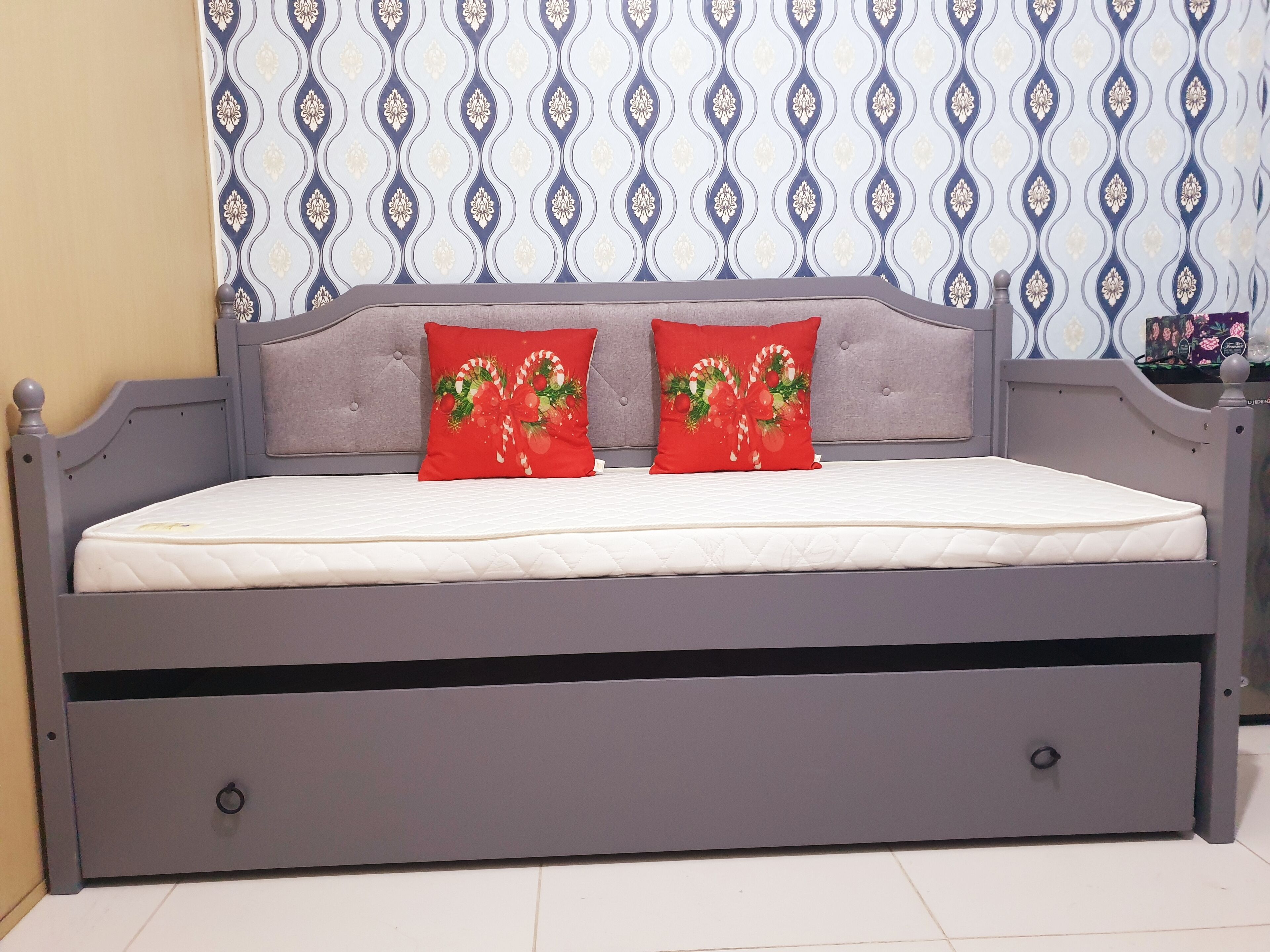 A bed with a grey headboard, two red pillows with Christmas decorations, and a patterned wallpaper in the background.