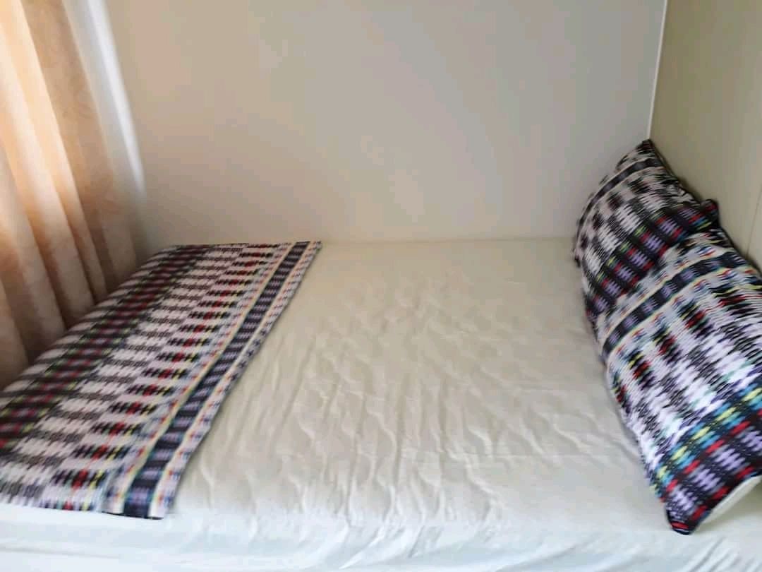A small, single-bed room with a plain white mattress, a colorful patterned blanket, and a matching pillow.