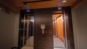 Zona de ascensor con paneles de madera, señal de prohibido fumar y símbolo de accesibilidad para sillas de ruedas.