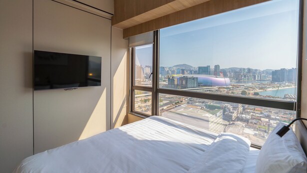 Una habitación de hotel con una cama, un televisor montado en la pared y un ventanal con vistas a la ciudad.