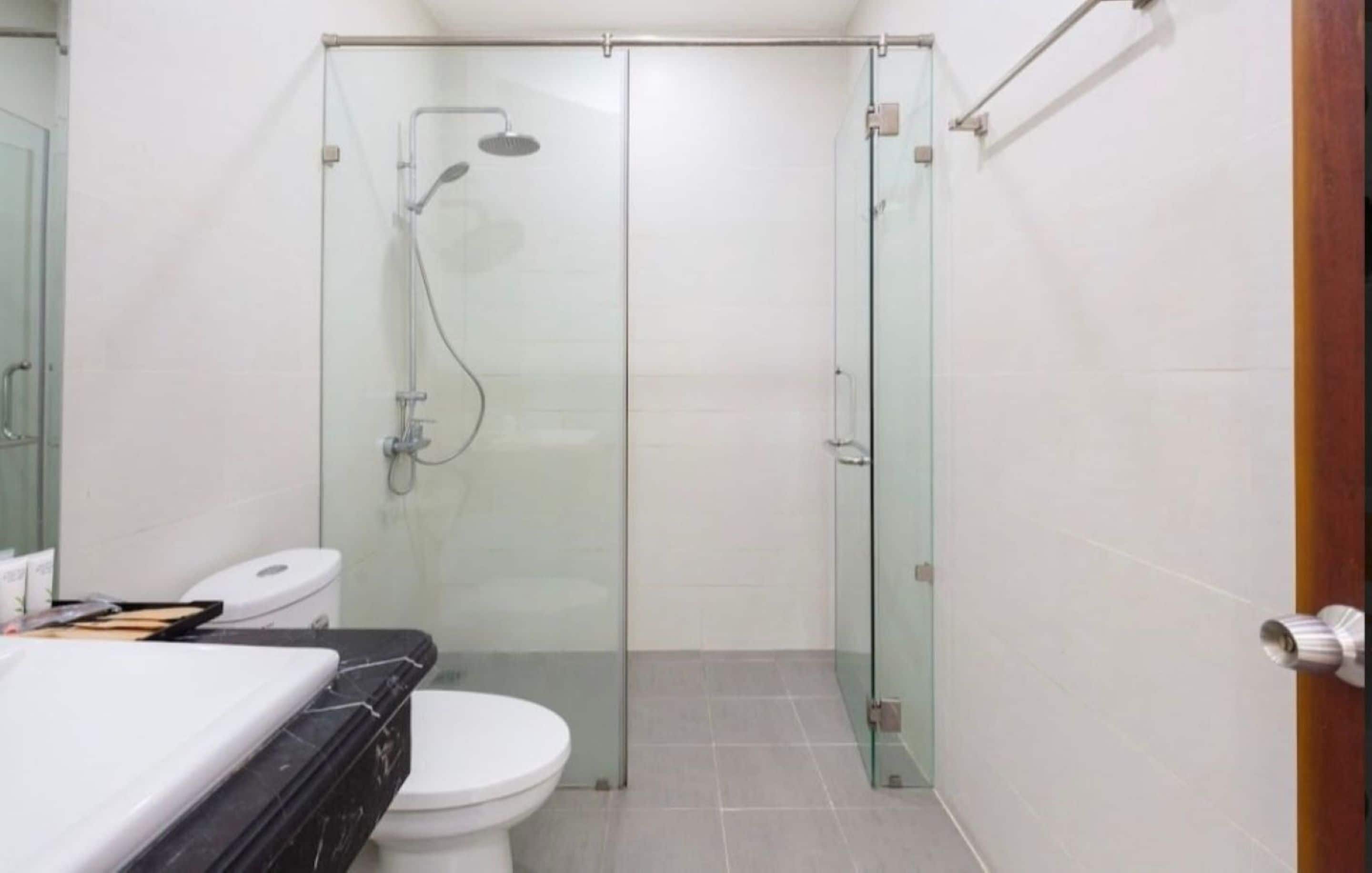 Un baño con ducha de vidrio, inodoro blanco y lavamanos de mármol negro.