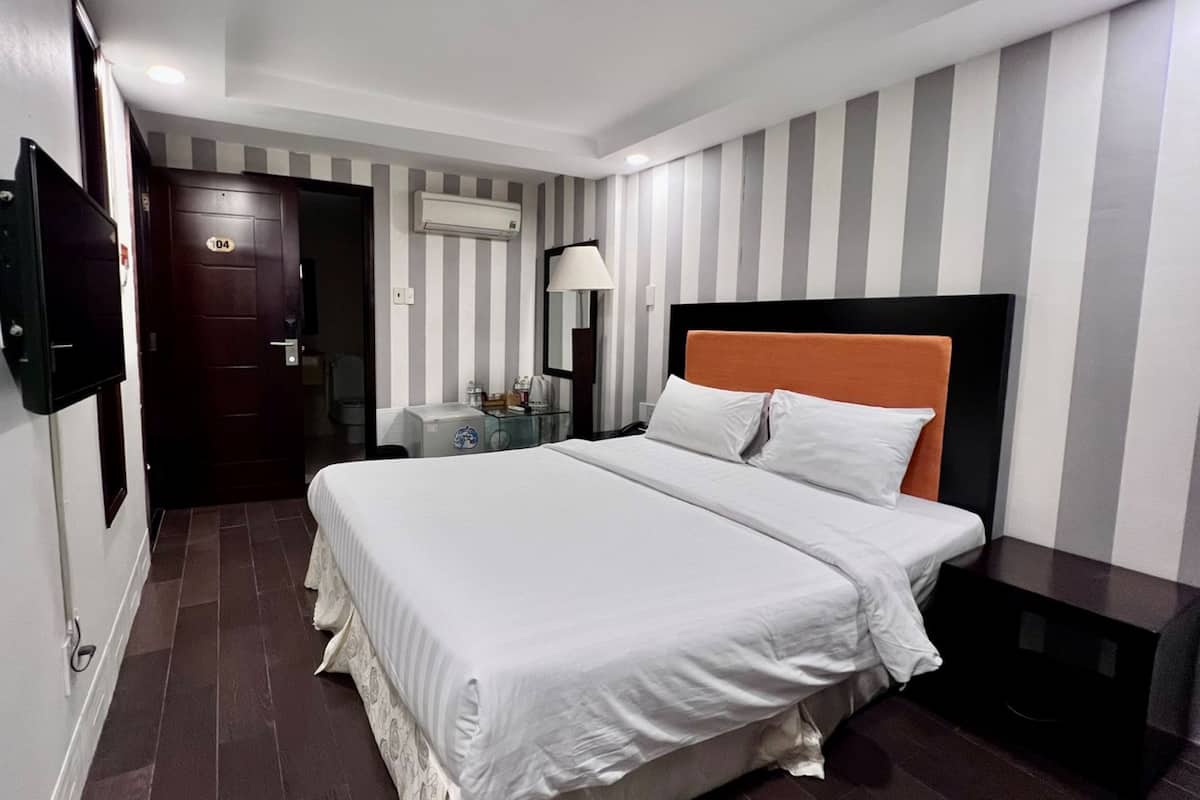 Een hotelkamer met een groot bed, een nachtkastje, een lamp en een deur met een nummer.