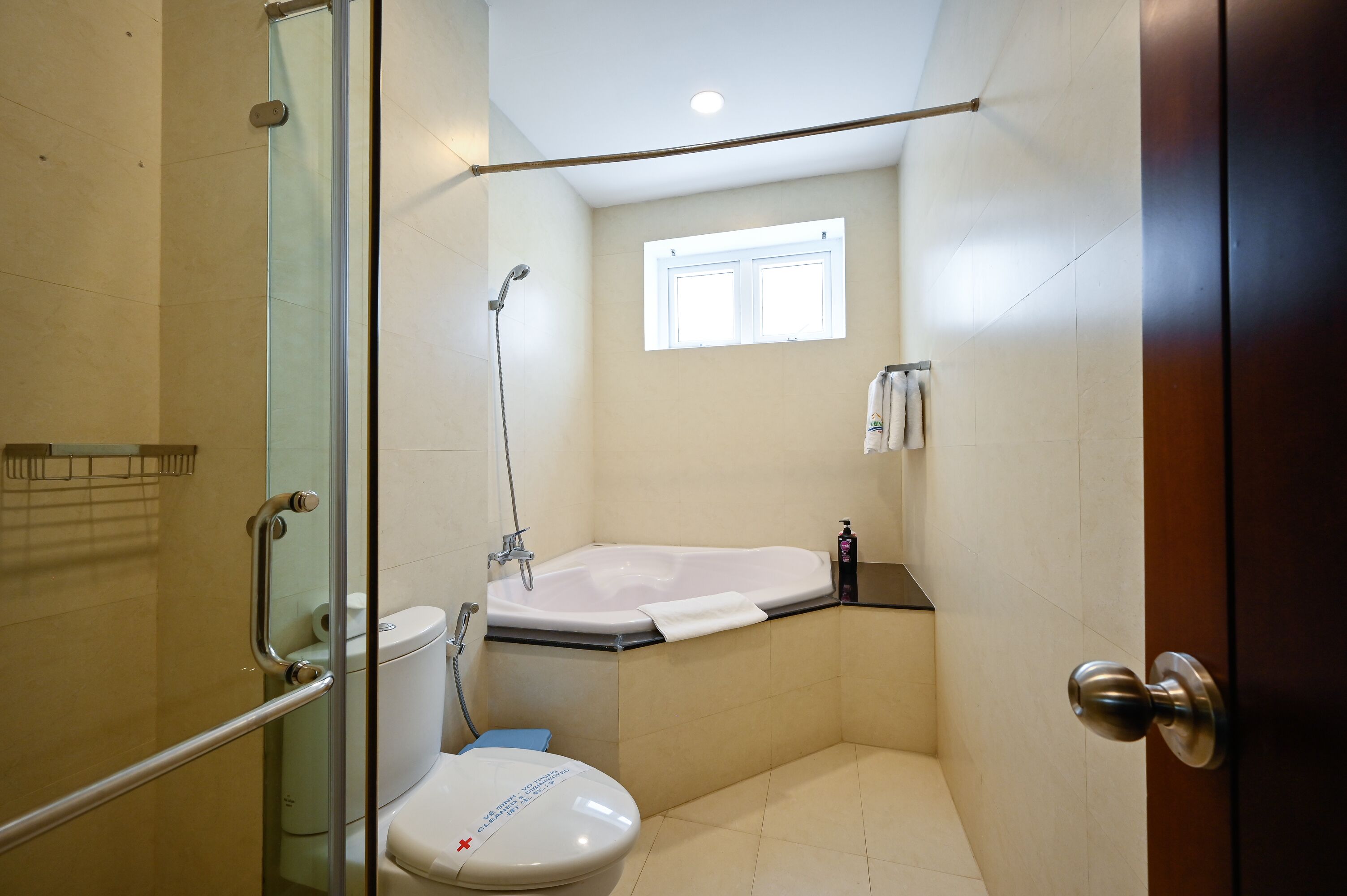 Une salle de bain dotée d’une douche à parois de verre, de toilettes blanches, d’une baignoire et d’une fenêtre laissant entrer la lumière naturelle.