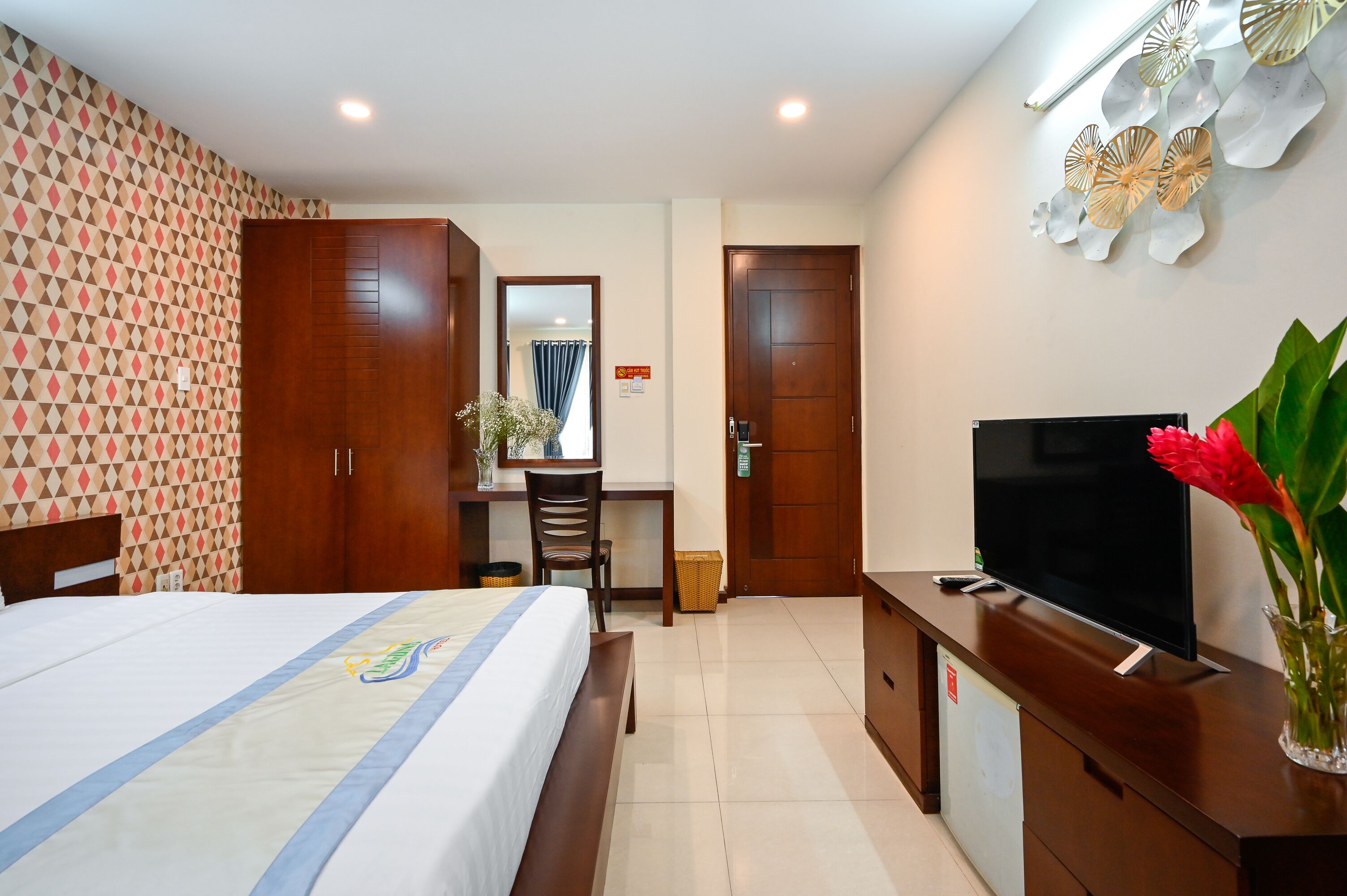 A hotel room with a bed, a desk, a television, and a wall with decorative panels.