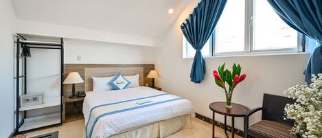 A hotel room with a bed, bedside lamps, a small table with flowers, a chair, and a window with curtains.