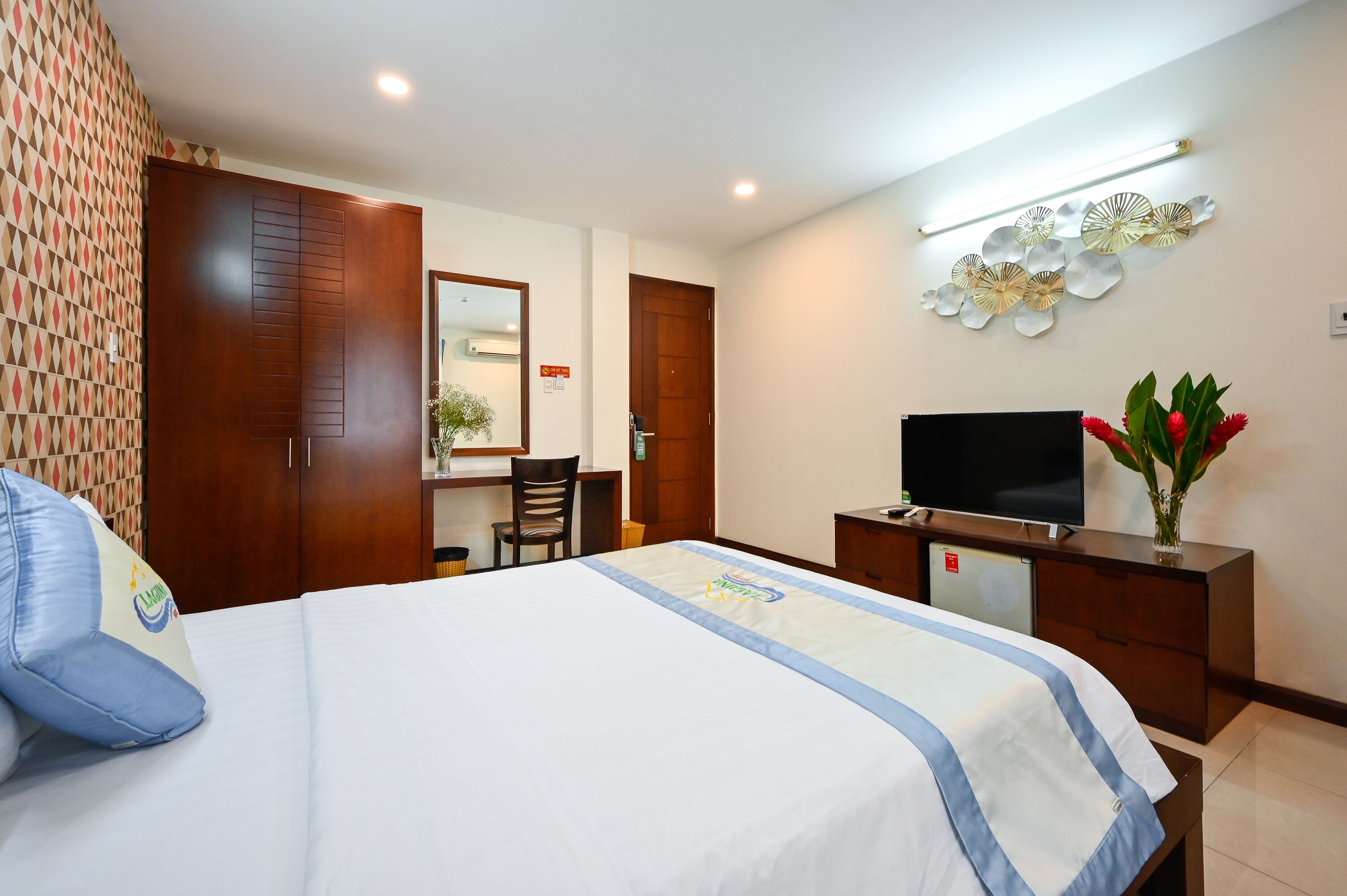 A hotel room with a bed, a desk, a television, and a decorative wall piece.