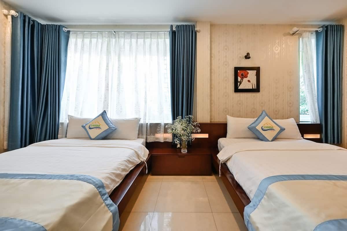 Een hotelkamer met twee bedden, een nachtkastje met een bloevas en een lijst aan de muur.