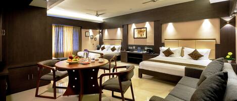 Habitación de hotel con cama, sofá, mesa de comedor con sillas, una pequeña cocina y baño.