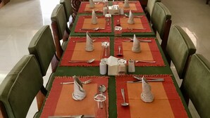 Un espace repas avec des tables dressées pour accueillir plusieurs convives, agrémenté de chaises vertes et de sets de table rouges.