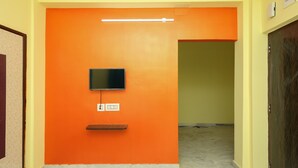 Ein Flur mit einer orangefarbenen Wand, einem daran befestigten Flachbildfernseher und einer Steckdose darunter.