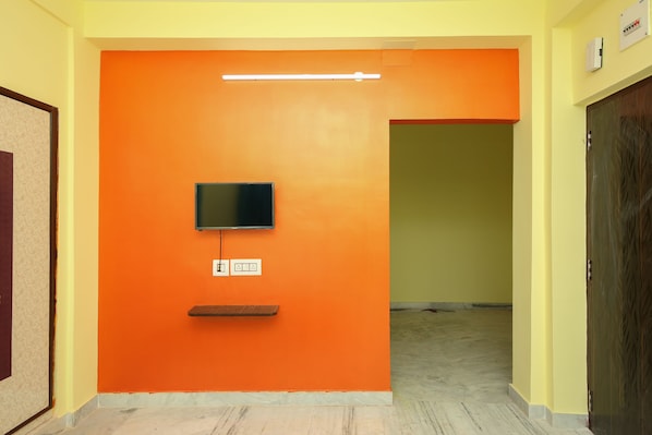 Um corredor com parede laranja, uma televisão de tela plana fixada nela e uma tomada logo abaixo.