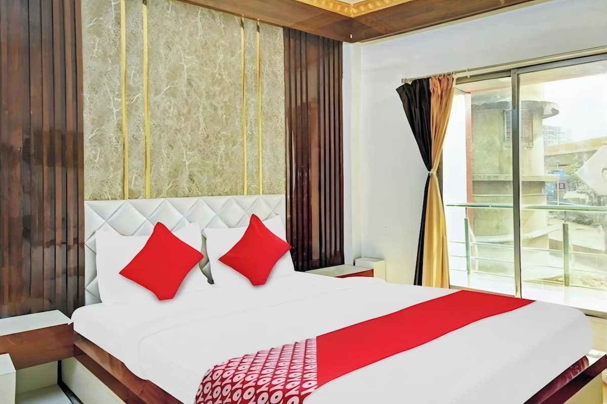 Quarto de hotel com cama, mesa de cabeceira, janela com cortinas e vista para prédios.