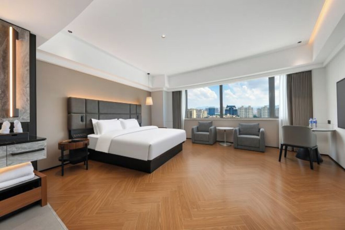 A modern hotel room with a large bed, a desk, a chair, and a city view.