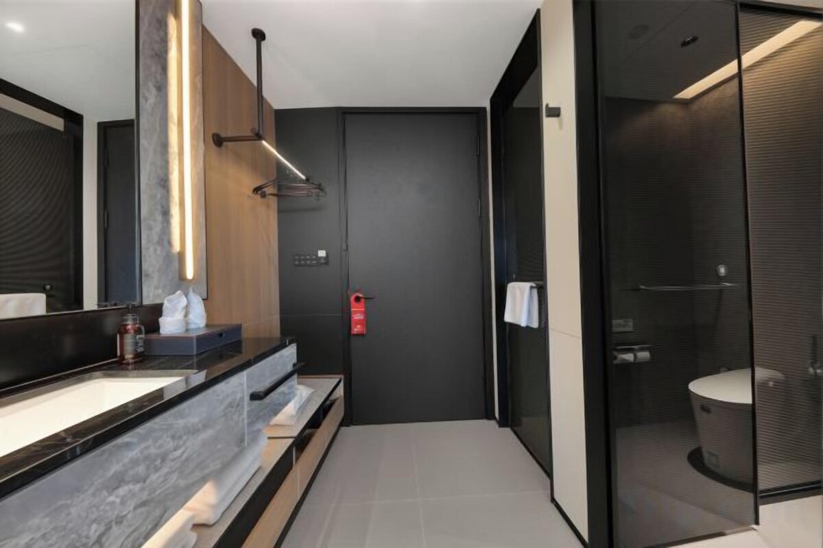 A modern bathroom with a glass shower enclosure, a dark wall, and a marble countertop.
