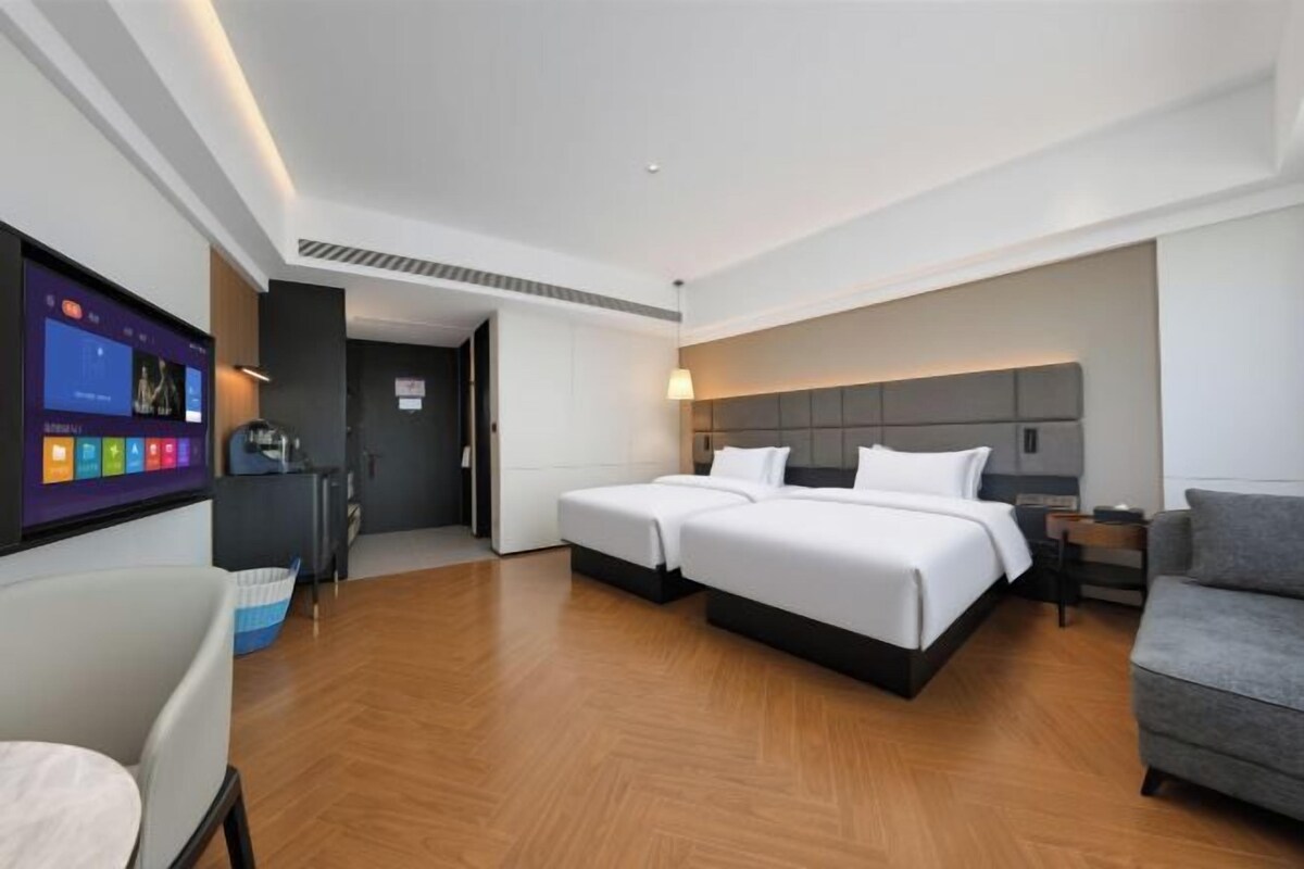 A hotel room with two beds, a desk, a chair, a TV, and a sofa.