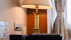 Una lámpara en una mesita de noche, con un enchufe y un libro a su lado.