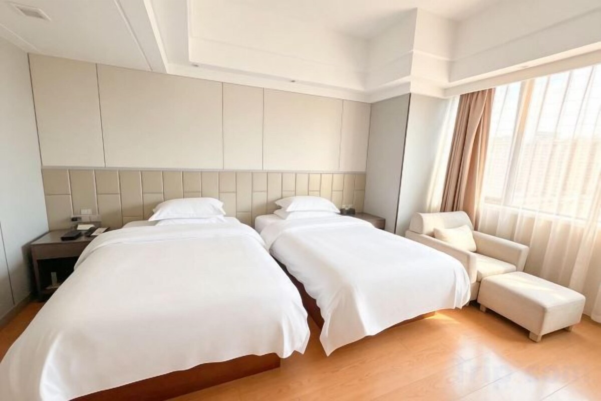 A hotel room with two beds, a nightstand, a chair, and a large window with curtains.
