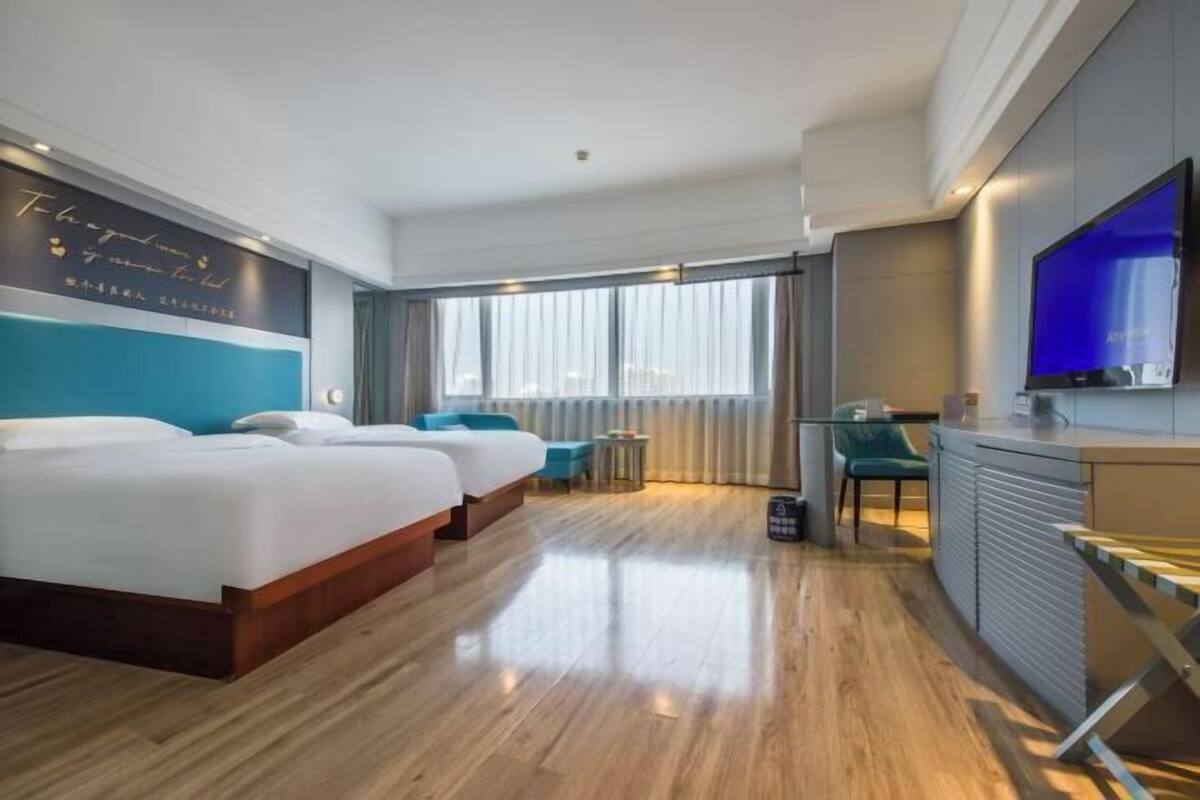 Ein Hotelzimmer mit zwei Betten, einem Schreibtisch, einem Fernseher und einem großen Fenster.