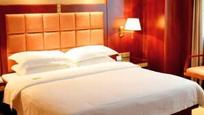 Habitación de hotel con una cama grande, una mesita de noche con lámpara y vistas al exterior.