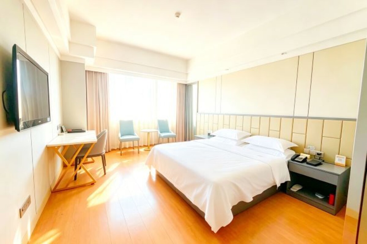 Una habitación de hotel con cama, escritorio, silla, televisor y mesita de noche.