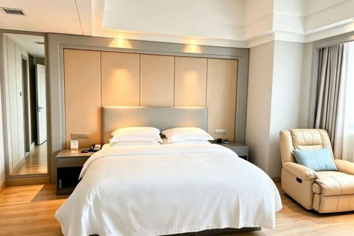 Una habitación de hotel con una cama grande, mesitas de noche, una silla y un espejo.