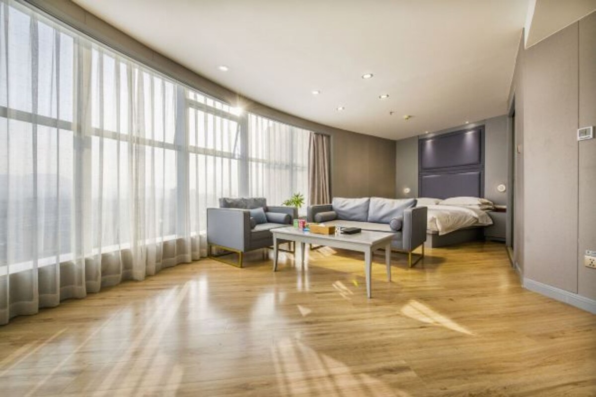 Uma sala de estar moderna com um sofá, mesa de centro e uma janela grande com cortinas leves.