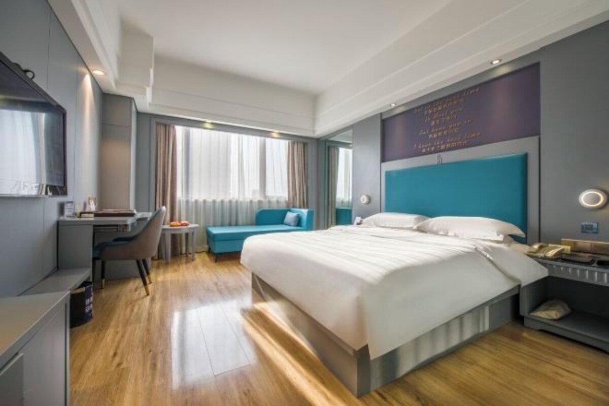A modern hotel room with a large bed, a desk, a chair, and a small table.
