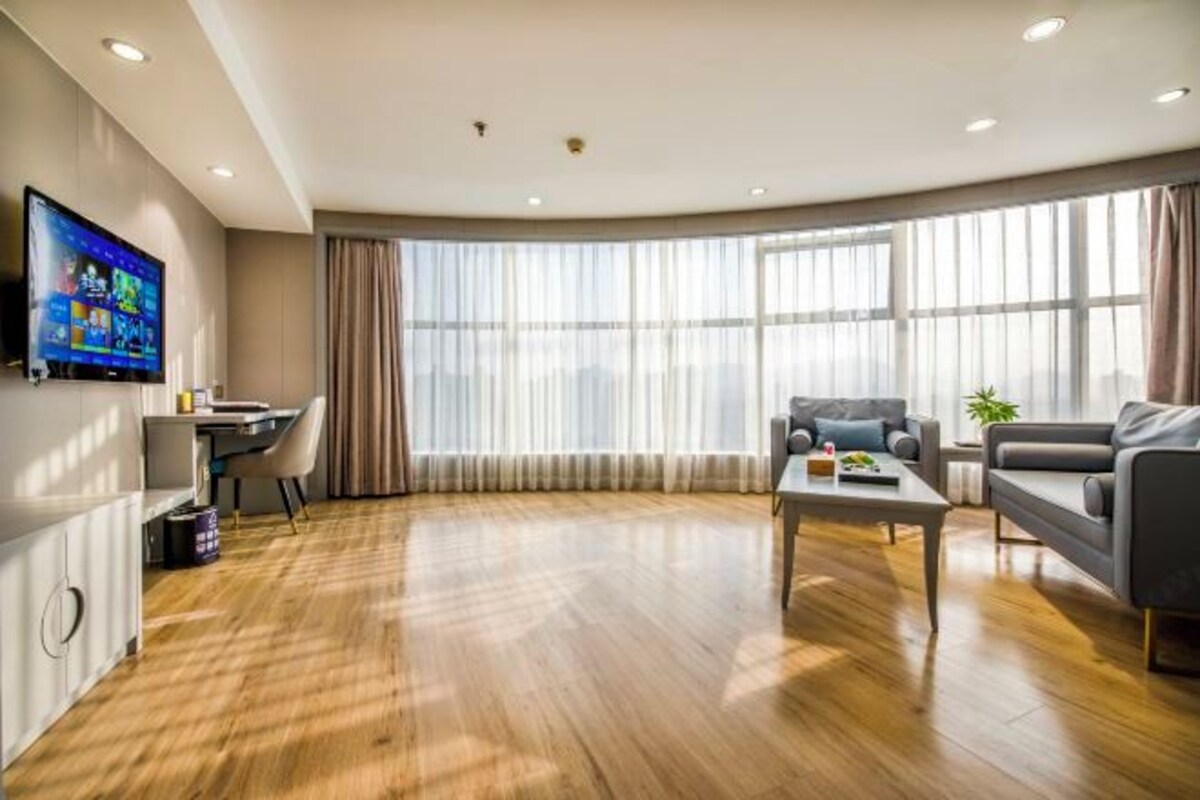 Una sala moderna con piso de madera, televisor de pantalla plana en la pared, un sofá, una mesa de centro y un comedor con una mesa pequeña y sillas.
