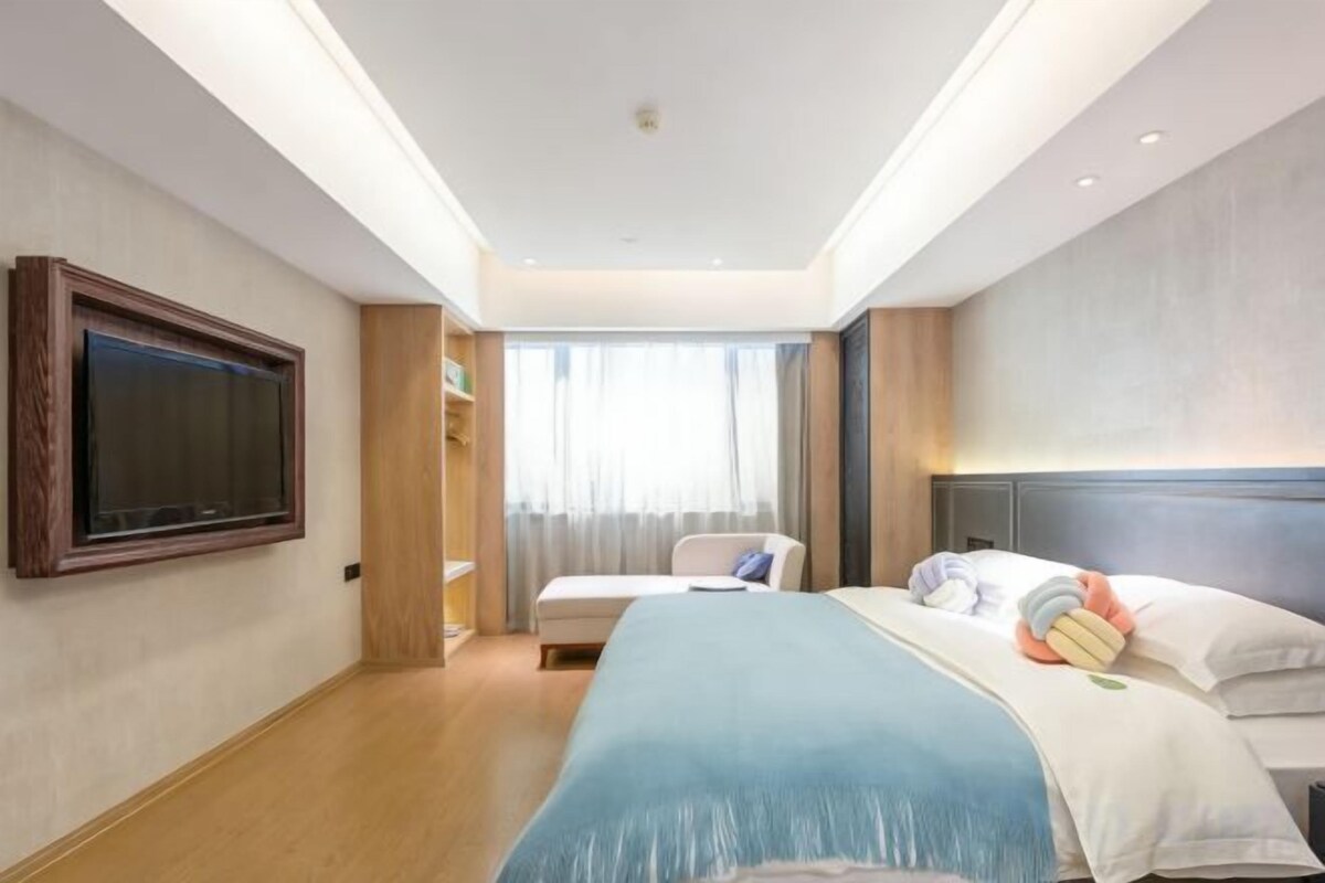 A hotel room with a bed, a TV, a desk, and a window with curtains.