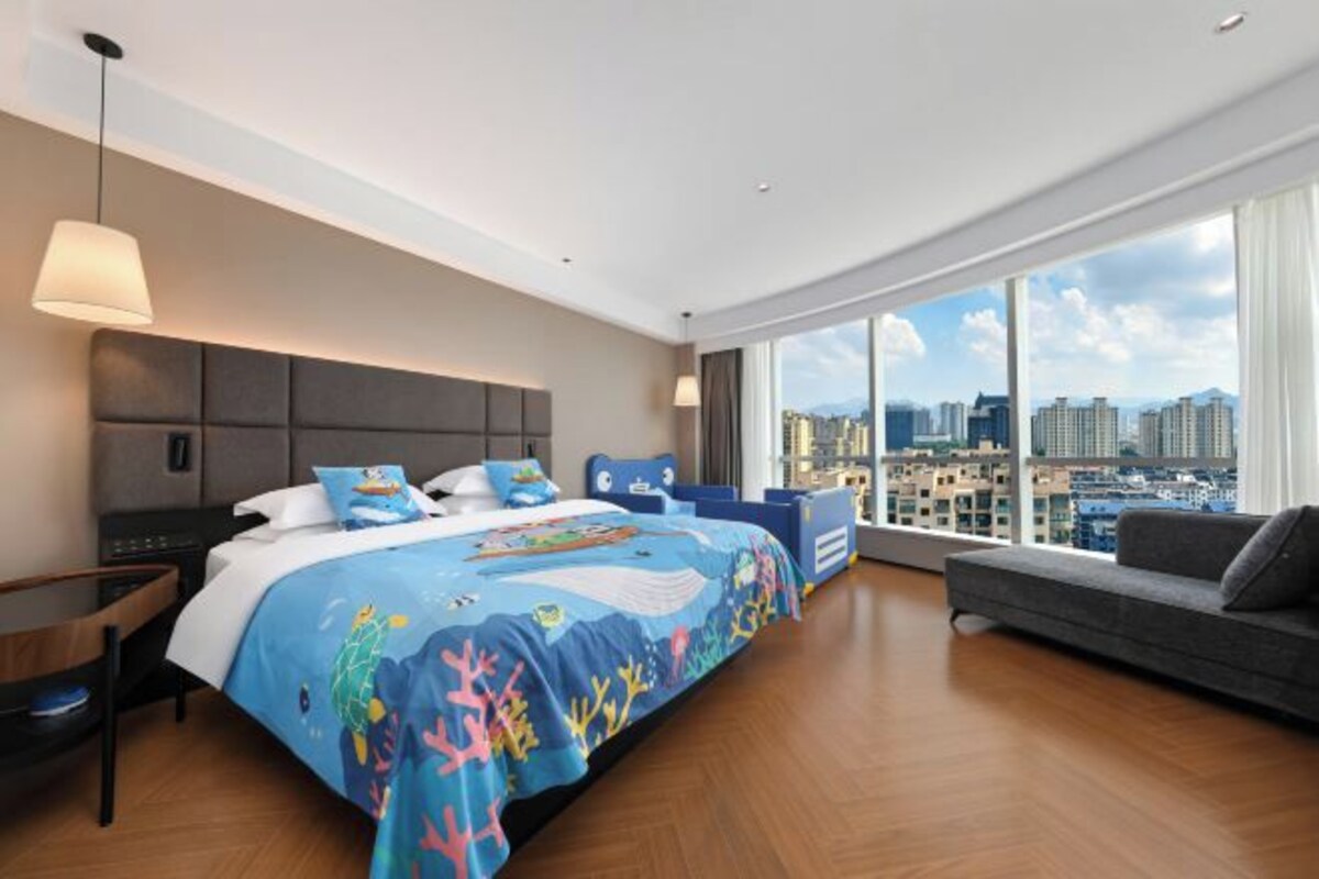 Habitación de hotel moderna con una cama grande, un sofá, un escritorio y vistas a la ciudad.