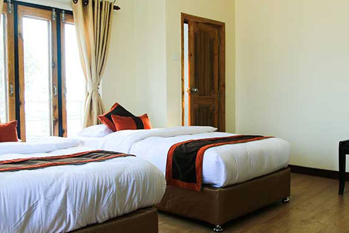 A hotel room with two beds, a wooden floor, and a door.