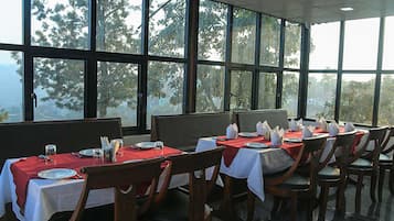 Un restaurante con mesas dispuestas para comer, ventanas amplias y vistas a árboles.